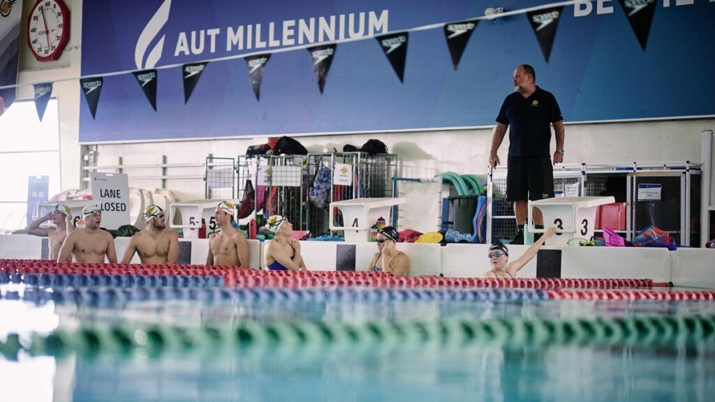 Coach standing by pool talking to athletes